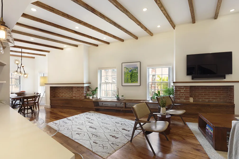 Open living and dining room in a Greenwich Village apartment with exposed wood ceiling beams, brick accents and wide-plank floors