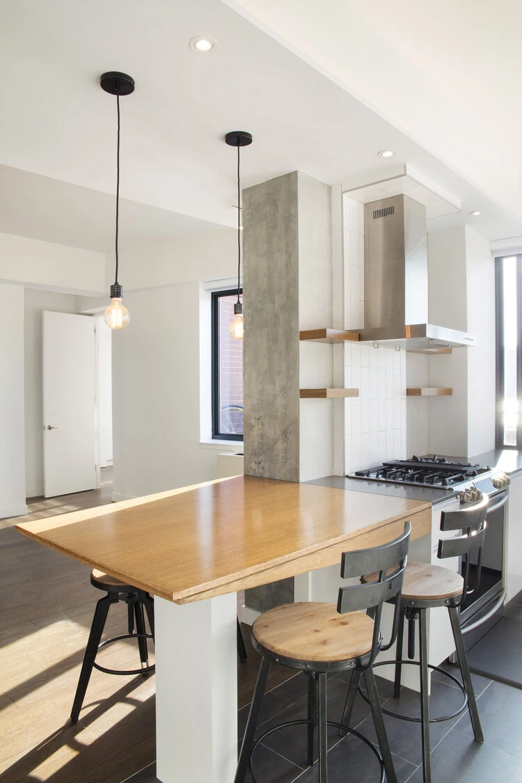 Wood counter seating beside the kitchen range and gray column in a CityLights apartment in Long Island City