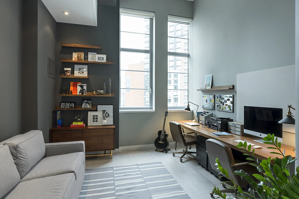 Arris Lofts home office in New York with a long wood desk, wall-mounted shelves and daylight from tall windows