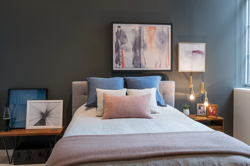 Dark painted bedroom accent wall behind an upholstered bed and framed artwork at Arris Lofts in New York