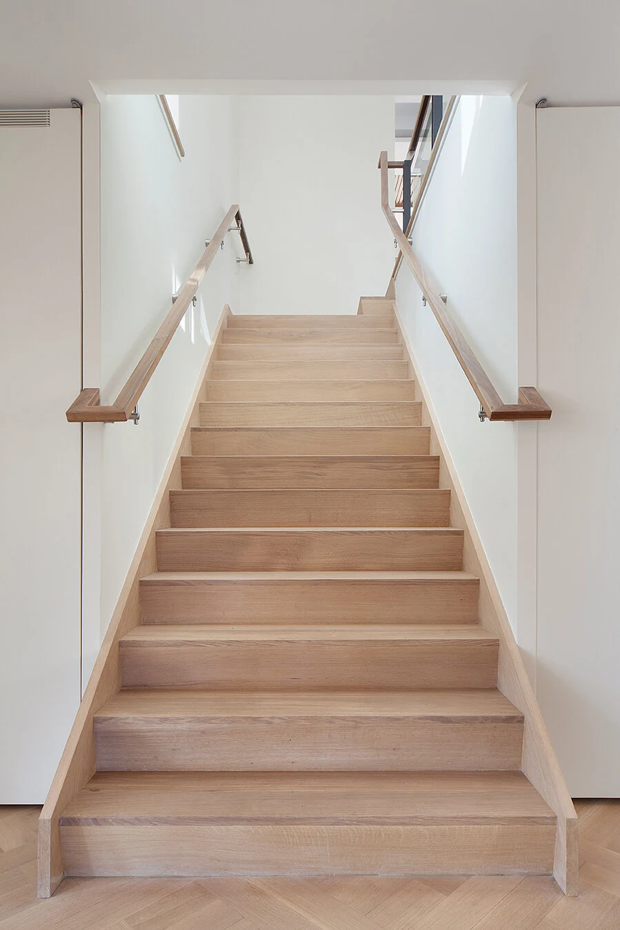Wood staircase with matching handrails between white walls in an Upper East Side apartment