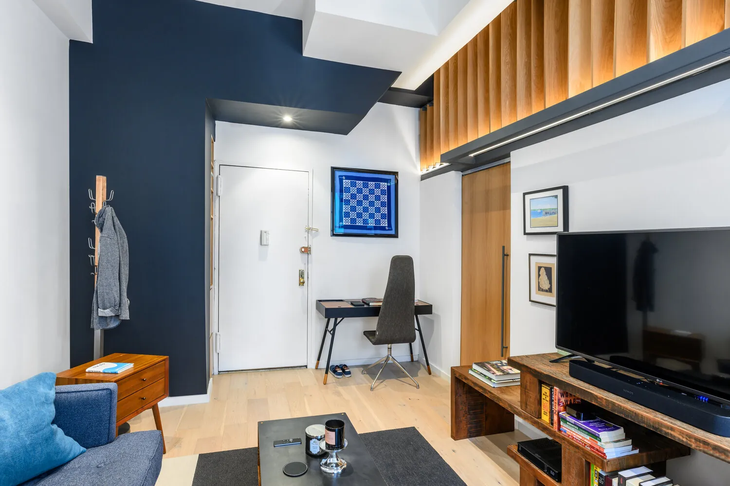 Lexington apartment living space in New York City with a dark entry wall, recessed lighting and a desk beneath the mezzanine