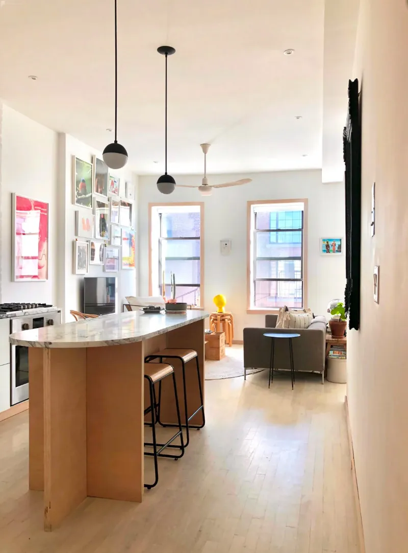 Kitchen island with a custom marble countertop opening into the living room of a renovated NoHo apartment by MELDNYC