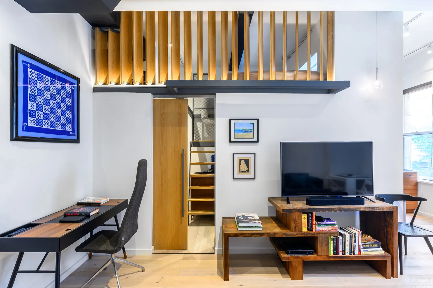 Wood-slat mezzanine railing above a television and office nook in the Lexington apartment in New York City
