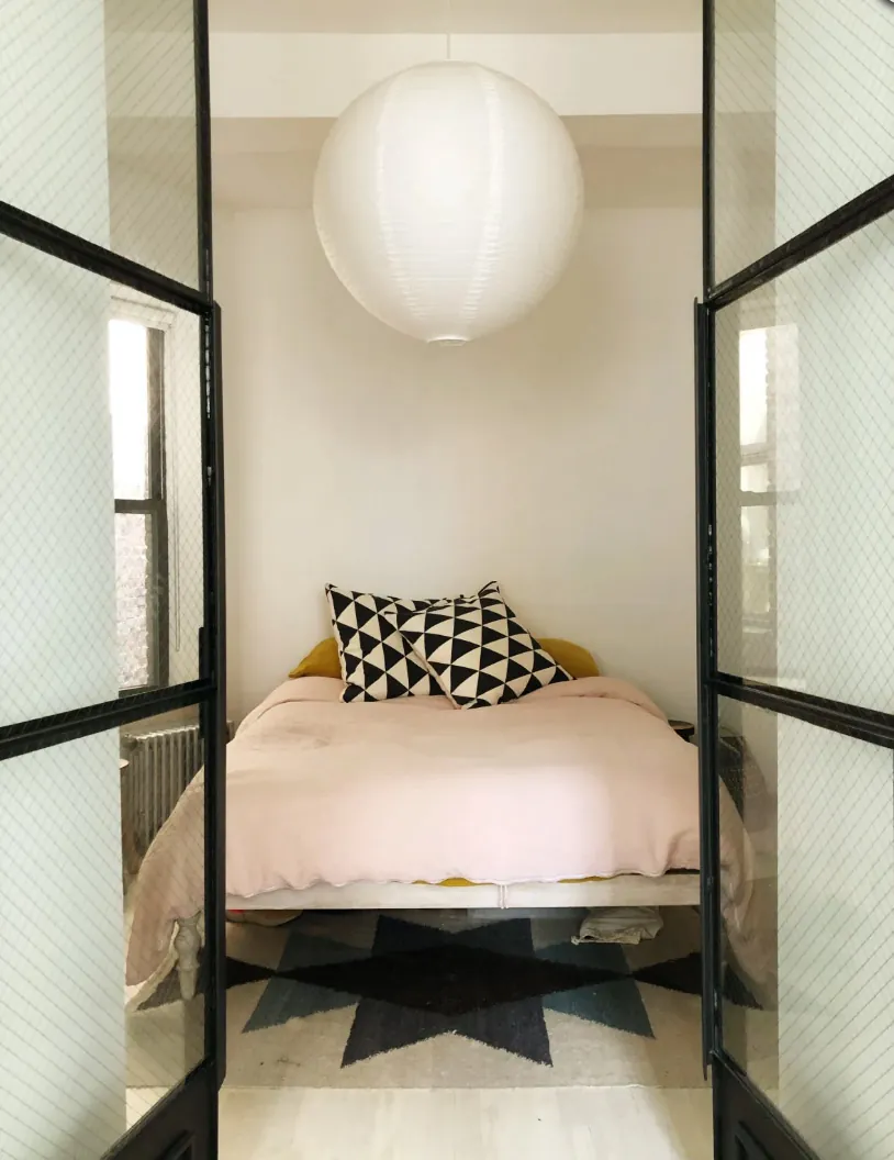 Bedroom seen through black steel framed French doors in a renovated NoHo apartment