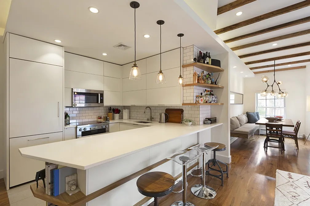 Open kitchen in a Greenwich Village apartment with a white waterfall island, pendant lights and open wood shelving