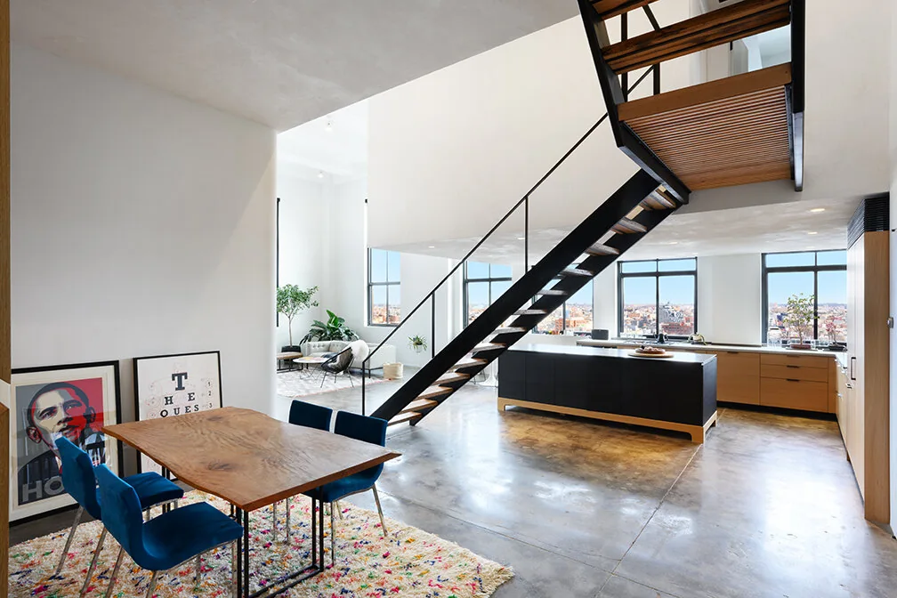 Dining table beneath an open-tread stair in a Williamsburg loft