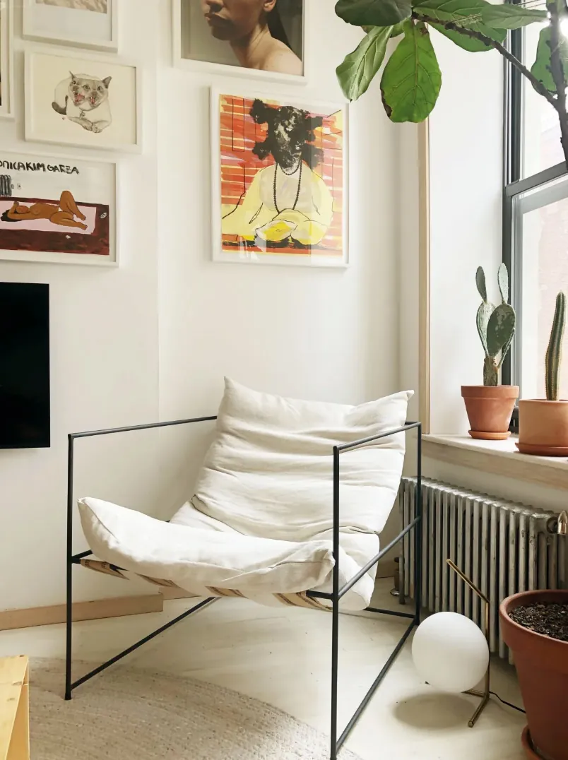 Lounge chair and radiator beside a plant filled window sill in a renovated NoHo apartment
