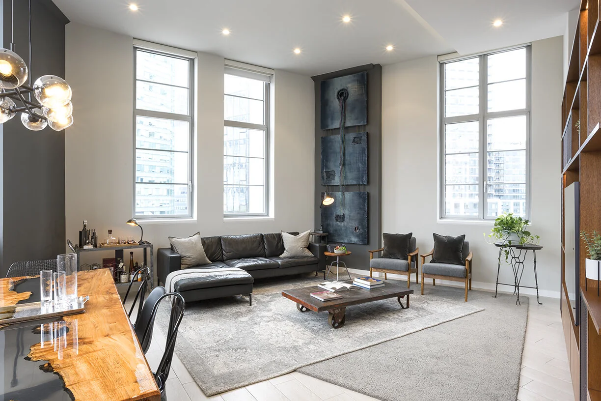 Open living and dining room at Arris Lofts in New York with tall windows, light flooring and a wood dining table