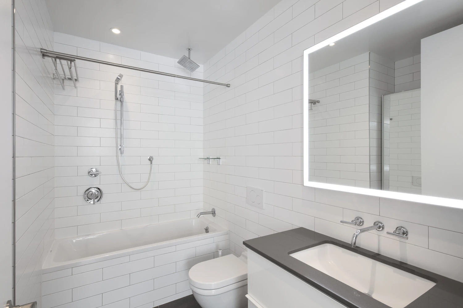 CityLights bathroom in Long Island City with white tiled walls, bathtub shower and an illuminated mirror above the vanity