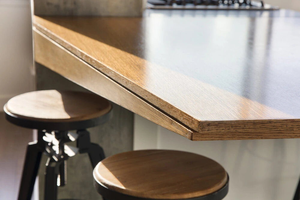 Close-up of the finished wood breakfast counter edge and round stools in a CityLights apartment in Long Island City