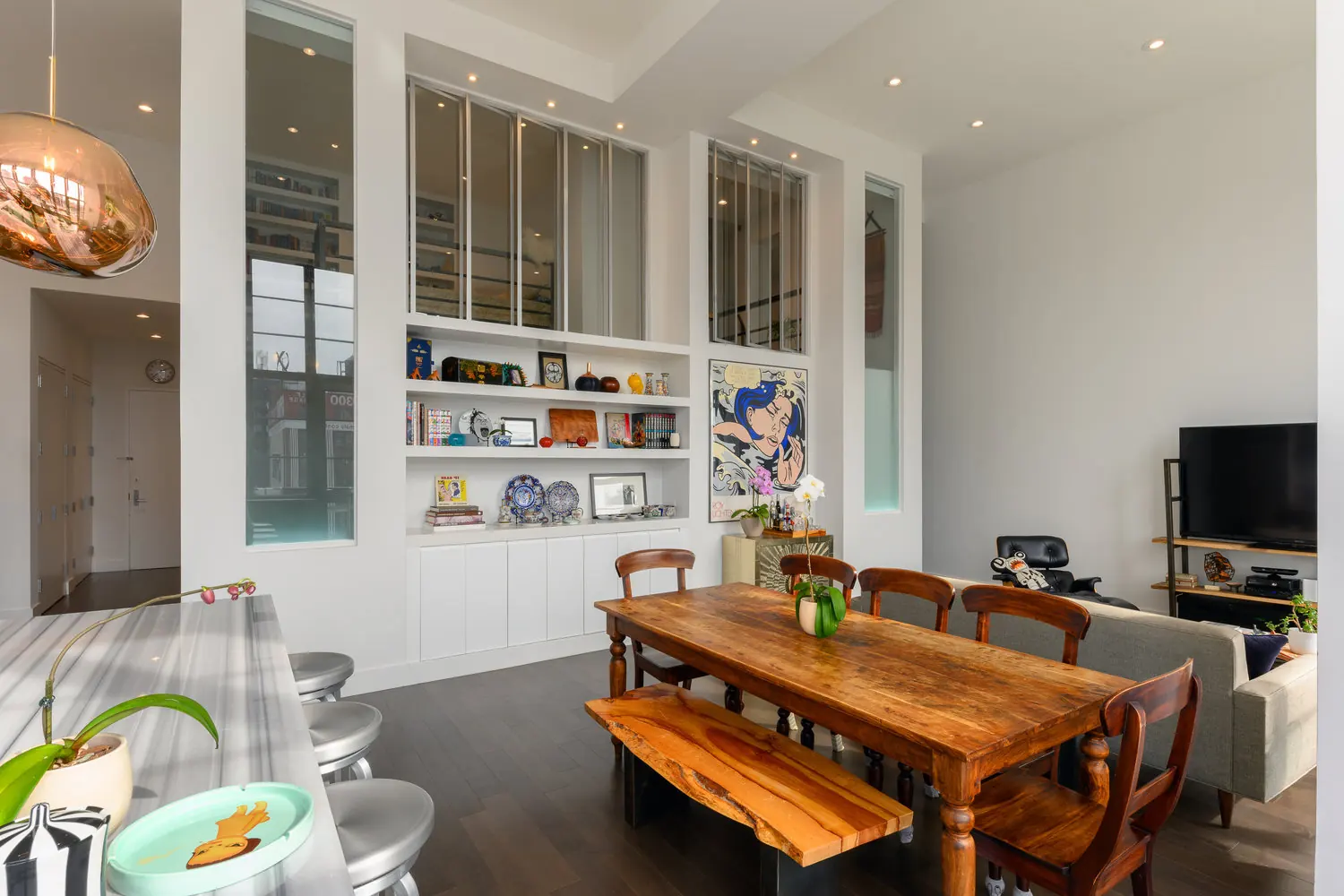 White built-in display shelving and cabinetry above a wood dining table in the Arris Lofts II apartment in Long Island City