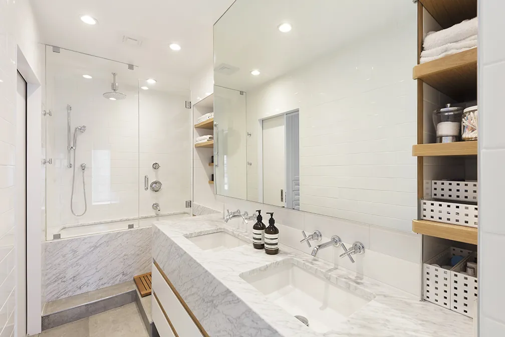 Marble bathroom in a Greenwich Village renovation with a double vanity, walk-in glass shower and wood shelving