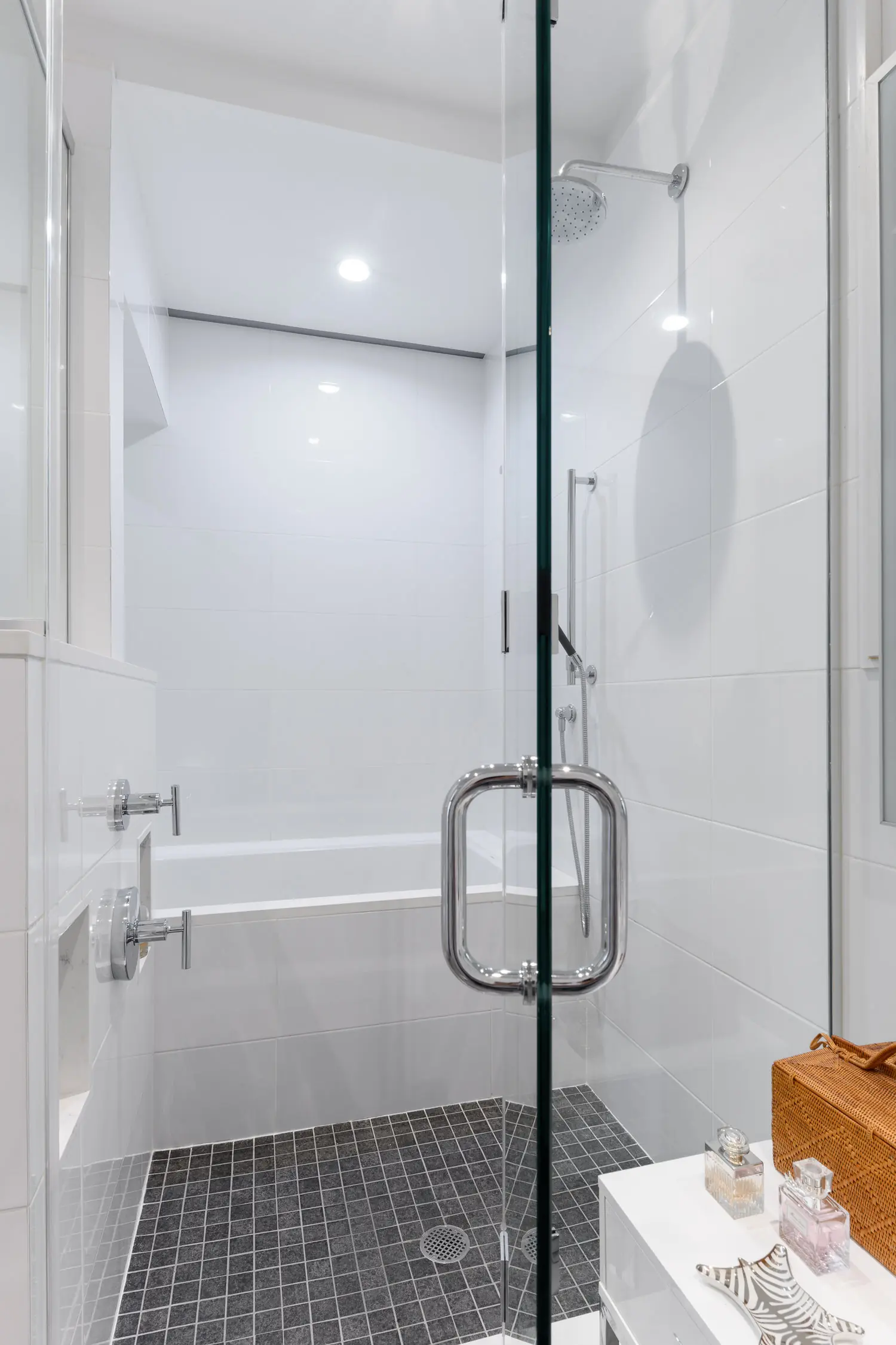 Glass shower enclosure with a metal handle, rainfall showerhead and dark mosaic shower floor at Arris Lofts II in New York