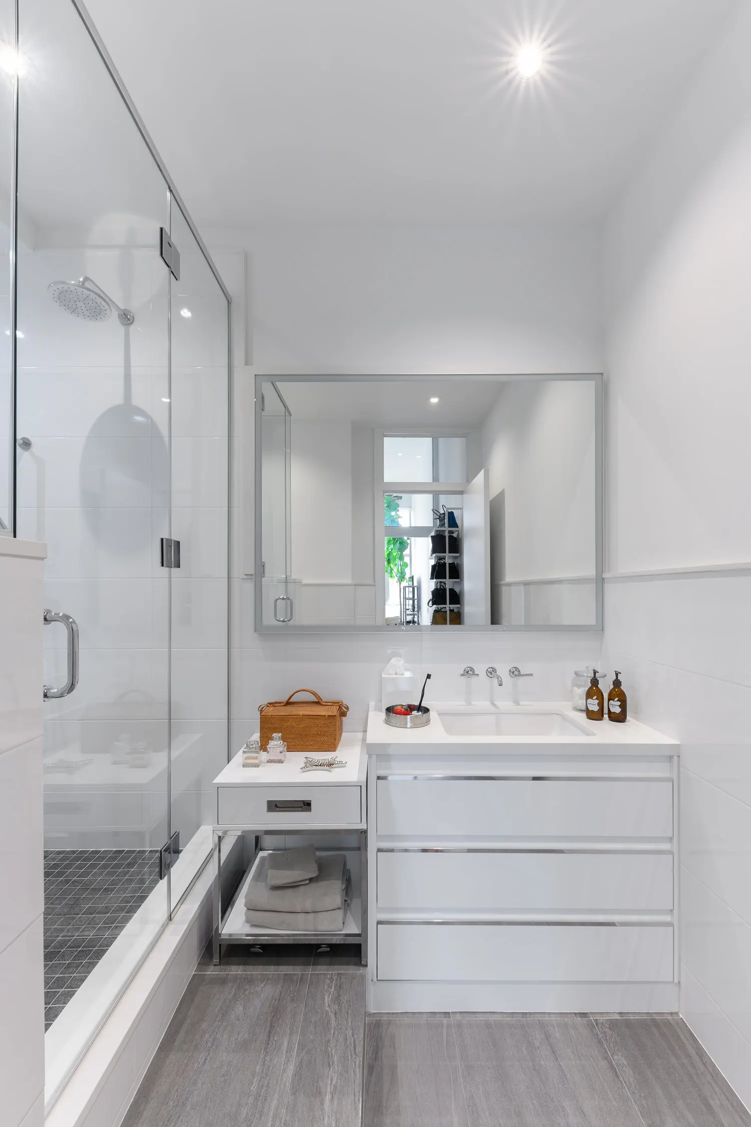 Arris Lofts II bathroom in New York with a white drawer vanity, broad mirror and glass shower beside gray floor tiles