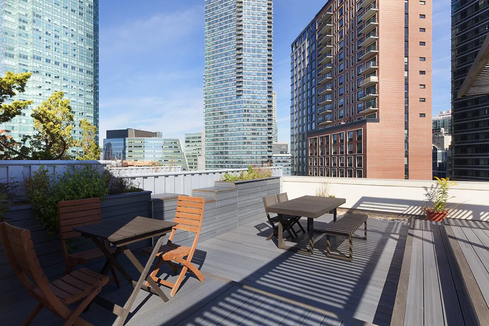 Rooftop dining area with deck seating and planters beside a custom pergola on Thompson Avenue
