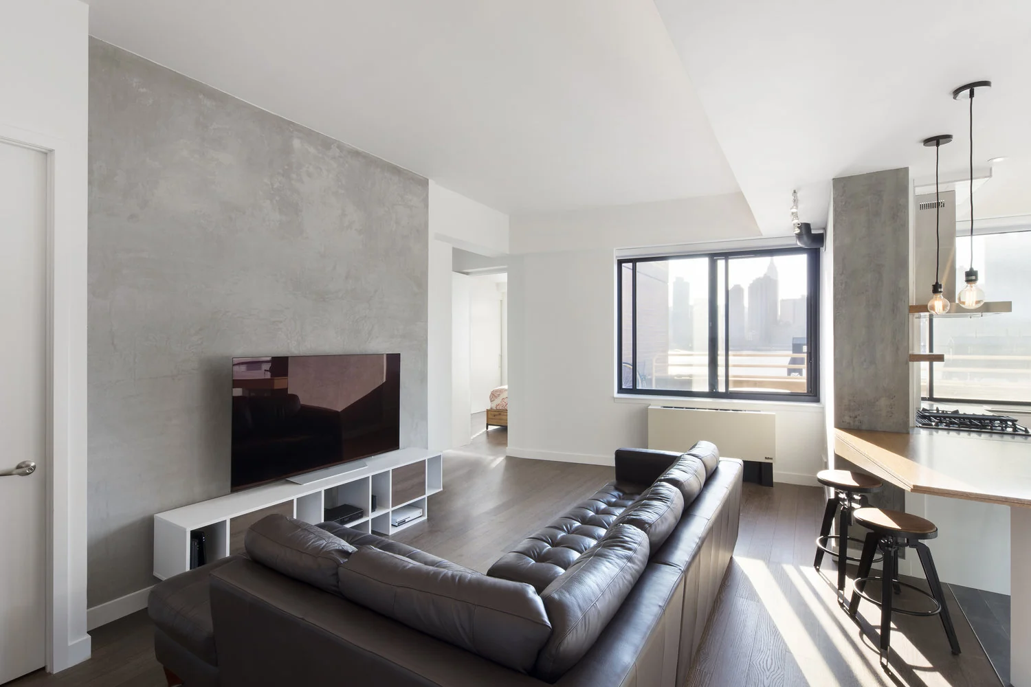 Sunlit CityLights living room in Long Island City with a dark sofa, textured gray feature wall and open kitchen
