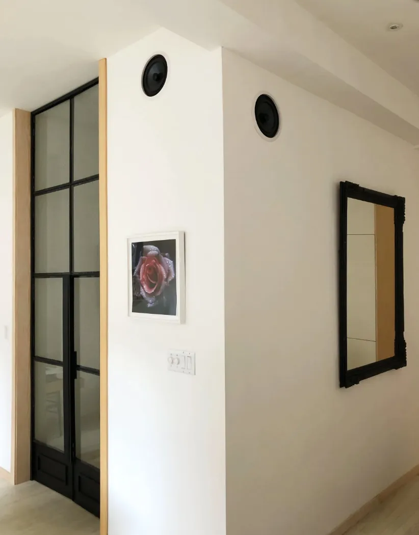 Hallway in a renovated NoHo apartment with a black steel framed glass door and flush in-wall speakers