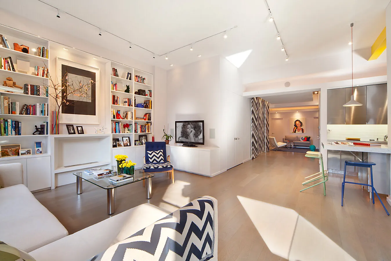 Open living room in a combined Greenwich Village apartment with built-in bookshelves, navy and white palette and a view through to the kitchen