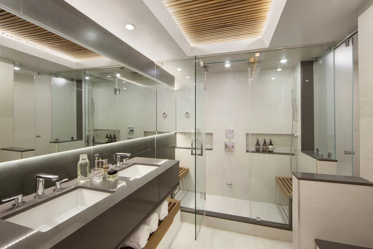 Soho bathroom in New York with a double vanity, illuminated mirror, glass shower and slatted ceiling detail