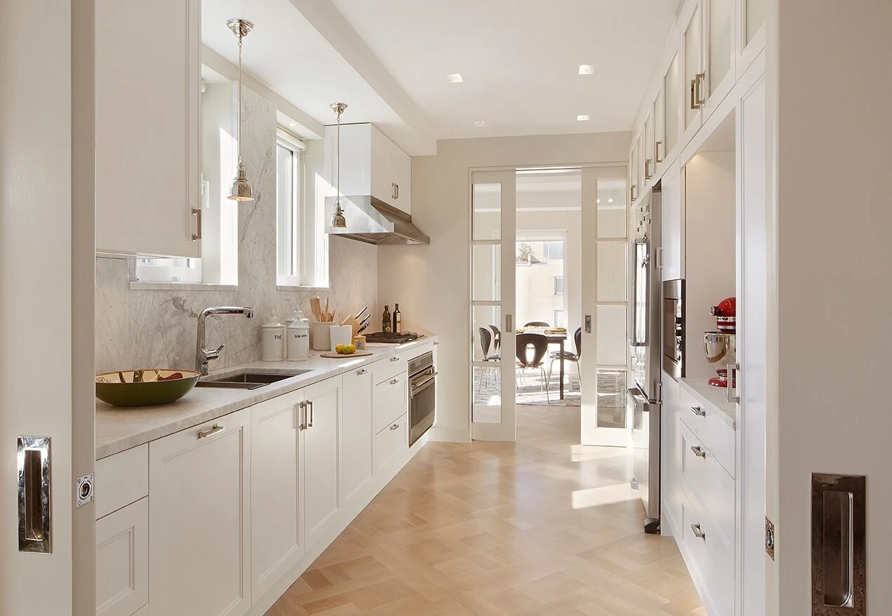 Upper East Side kitchen in New York with white cabinetry, veined backsplash, pendant lights and herringbone wood flooring