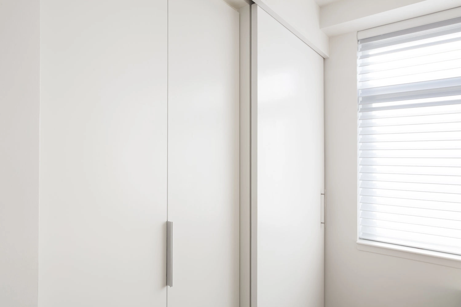 Full-height white closet cabinetry with long metal handles beside a shaded window in a CityLights apartment