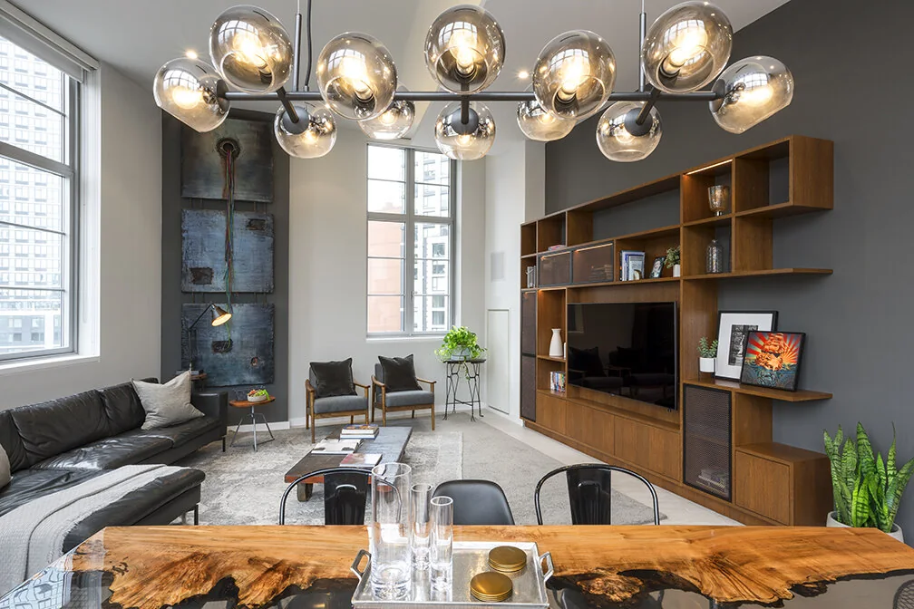 Arris Lofts living room in New York with a built-in wood media wall and glass globe chandelier above the dining table
