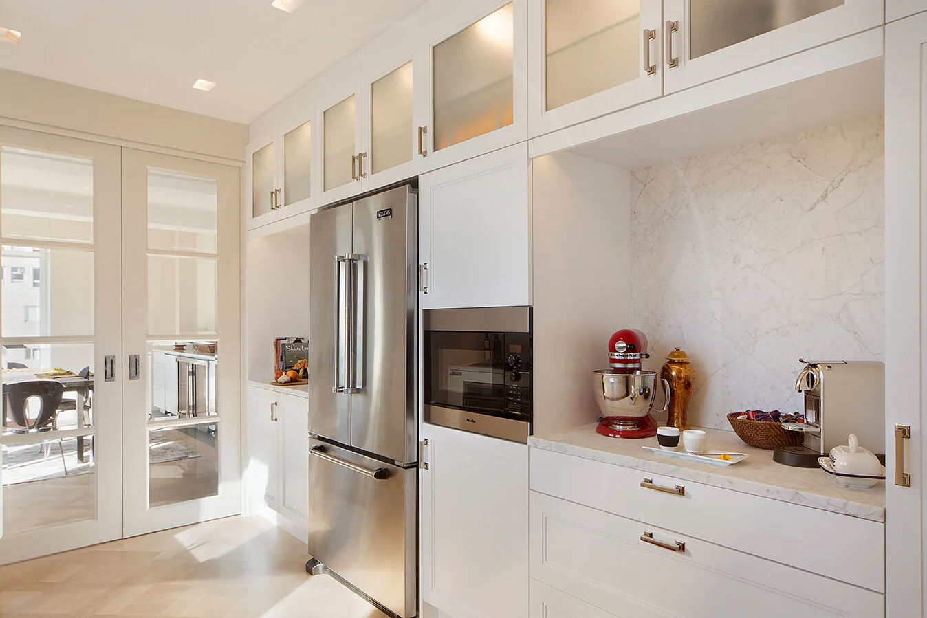 White kitchen storage with glass-front upper cabinets and stainless steel appliances on the Upper East Side