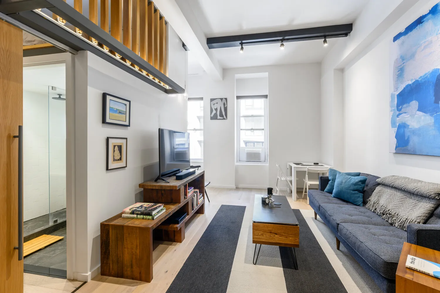 Lexington living room in New York City with a gray sofa, pale wood flooring, track lighting and a wood-slat mezzanine above