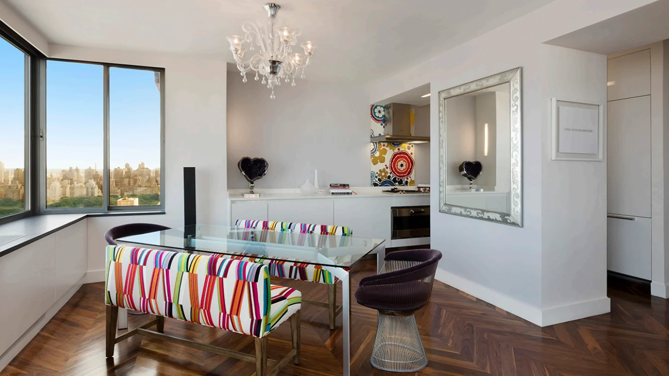 Upper West Side dining area in New York with corner windows, a glass table, striped seating and a kitchen beyond