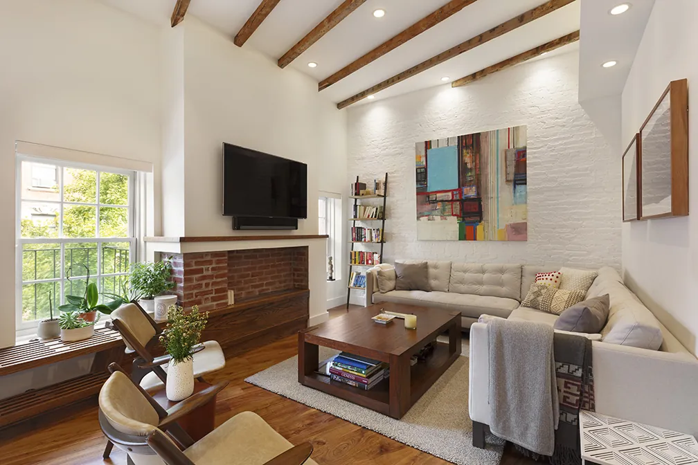 Living room in a Greenwich Village renovation with a brick fireplace, exposed beams and a deep window bench