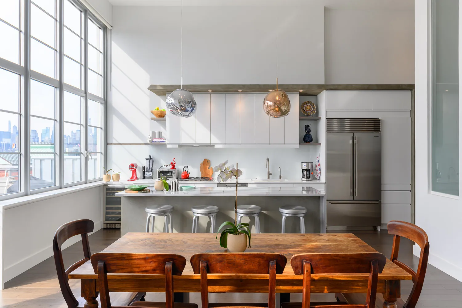 Arris Lofts II kitchen in Long Island City, New York with white cabinets, an island, metal stools and globe pendant lights beside tall windows