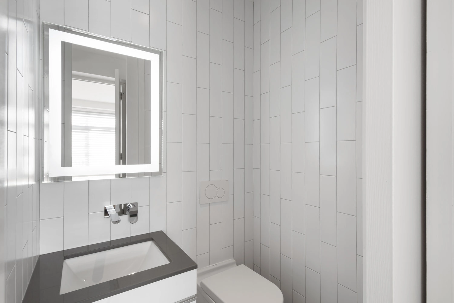 CityLights bathroom vanity in New York with a dark countertop, wall-mounted faucet and illuminated rectangular mirror