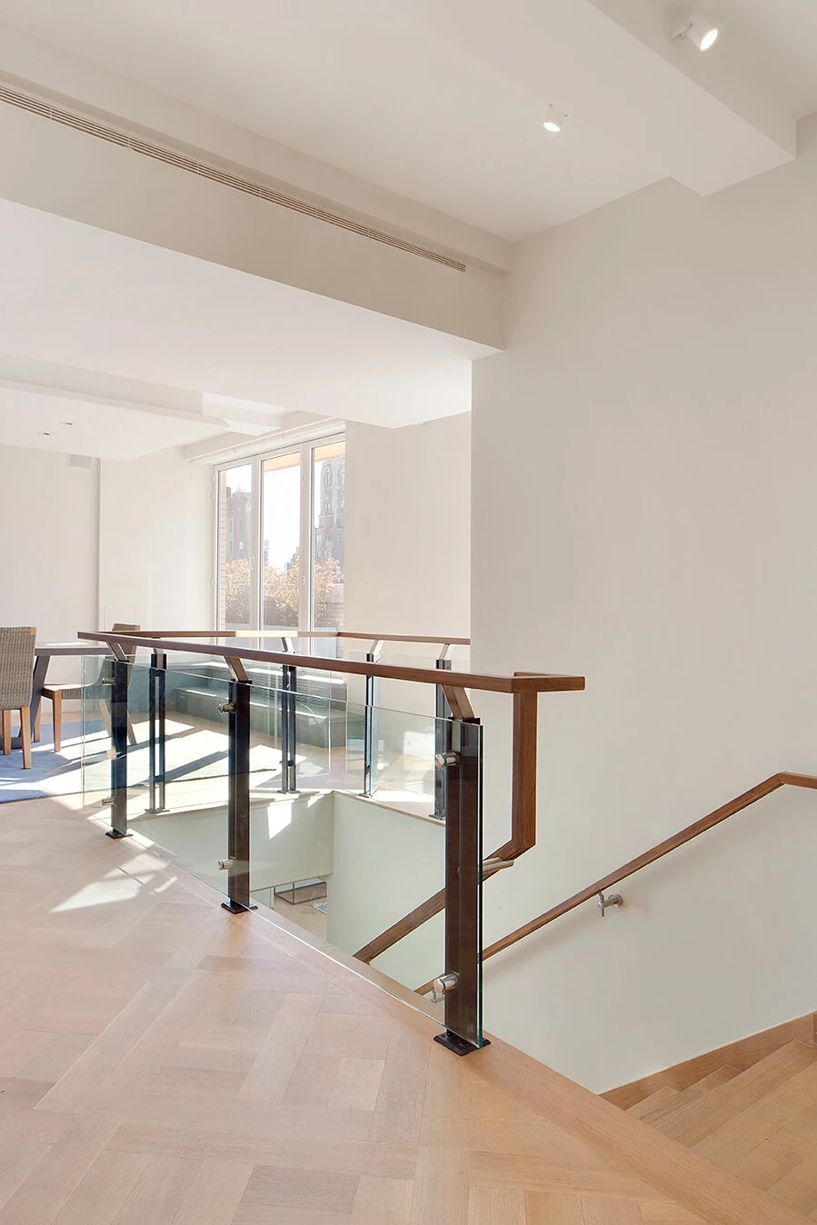 Glass-railed stair landing with a wood handrail and herringbone flooring on the Upper East Side
