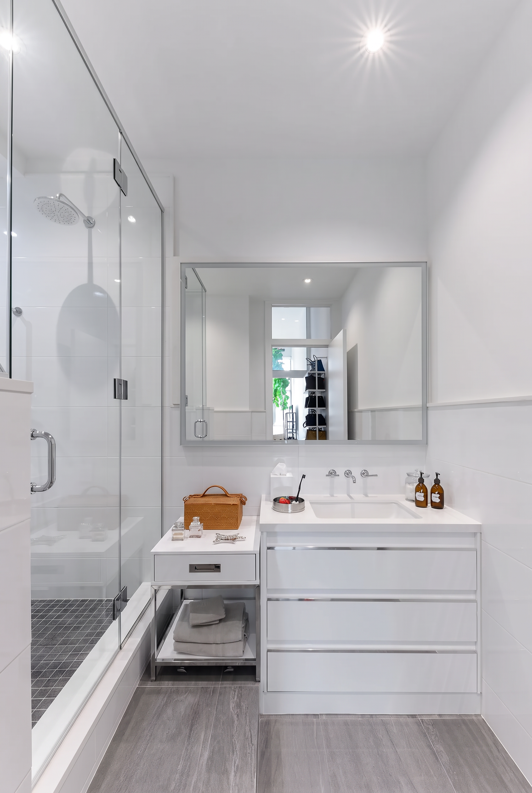 Arris Lofts II bathroom in New York with a white drawer vanity, broad mirror and glass shower beside gray floor tiles