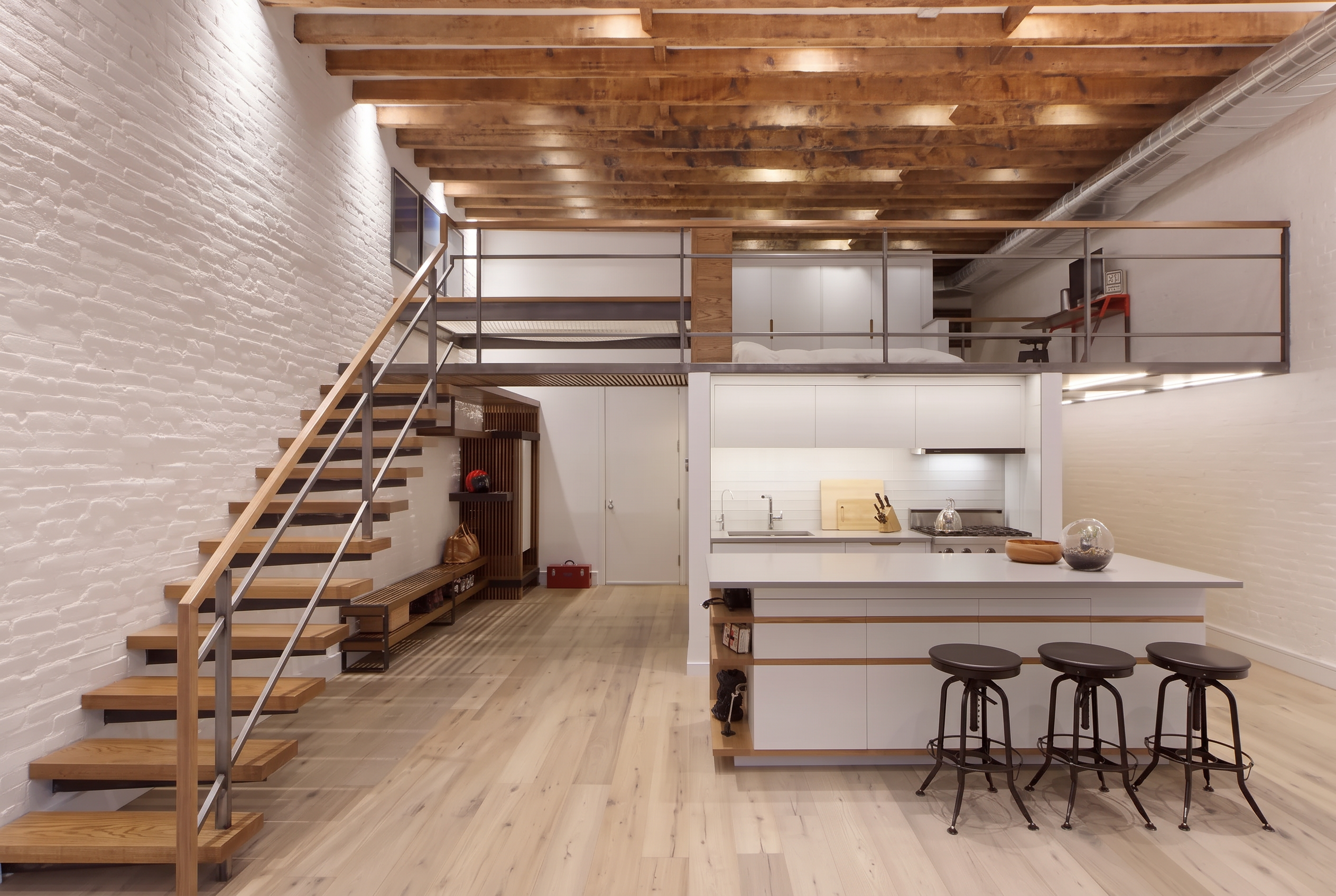 Open Soho loft in New York with exposed wood beams, white brick walls, a staircase and mezzanine above the kitchen